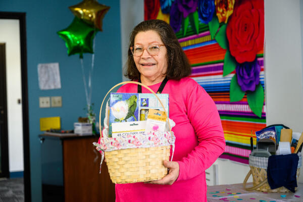 A Hispanic woman holds a basket of donated craft supplies at our senior social program