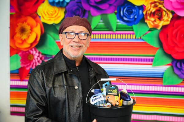 A Latino man holds a basket of donated cleaning supplies at our senior social program
