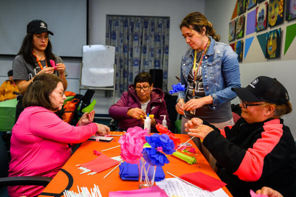Two of our staff members help three senior Hispanic women with a craft project
