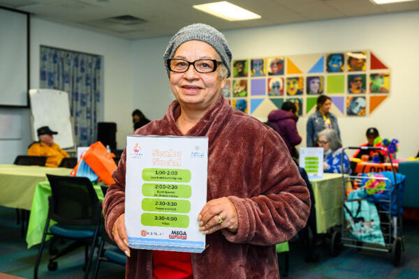 A Hispanic woman holds up an invitation to our senior social program
