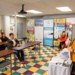 Staff member speaking with a participant at a table with informational materials during a job-fair event
