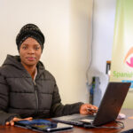 Adult learner using a laptop at a career-training booth, with a staff member nearby