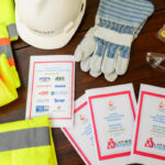 A table displays safety gear including a hard hat, gloves, safety glasses, earplugs, and yellow vests, alongside several “Latino Construction Program” welcome pamphlets.