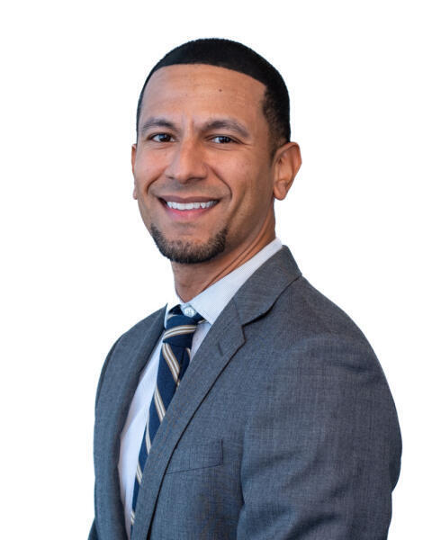 A man wearing a gray suit, white shirt, and striped tie smiles while posing for a professional headshot against a plain white background.