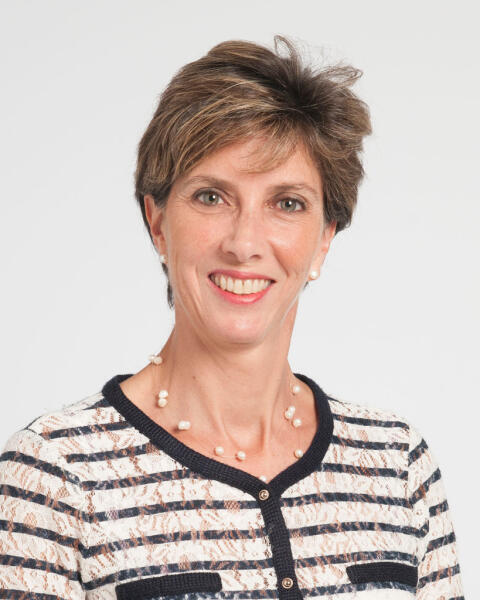 A woman with short brown hair wearing a striped cardigan and a pearl necklace, smiling against a plain white background.